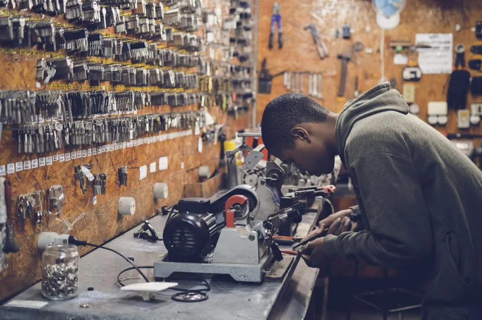 A locksmith cutting a key at a workbench in front of a wall of key blanks